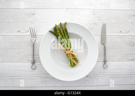 Draufsicht auf frischem grünen Spargel auf einem weißen Teller über einen Retro-Holz-Hintergrund Stockfoto
