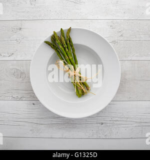 Draufsicht auf frischem grünen Spargel auf einem weißen Teller über einen Retro-Holz-Hintergrund Stockfoto