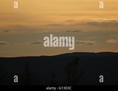 Himmel mit verschiedenen Schattierungen von Orange über ein Bergsilhouette in Schweden. Stockfoto