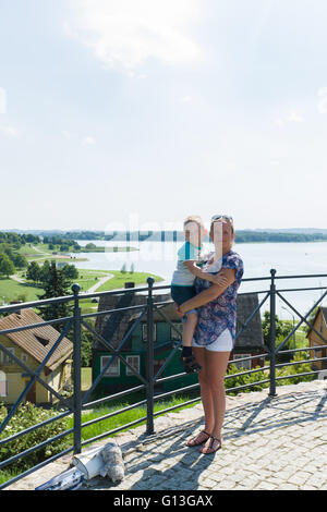 junge Mutter mit dem kleinen Kind an Händen gegen eine Kleinstadt Stockfoto