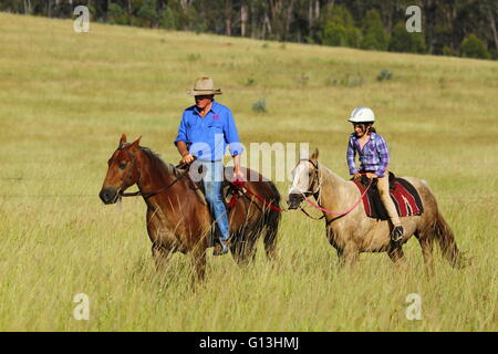 Ein Großvater und junge Enkelin Reitpferde auf einem Vieh-Grundstück in der Nähe von Eidsvold in Queensland, Australien. Stockfoto