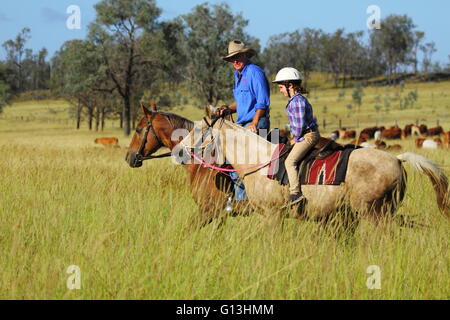 Ein Großvater und junge Enkelin Reitpferde auf einem Vieh-Grundstück in der Nähe von Eidsvold in Queensland, Australien. Stockfoto