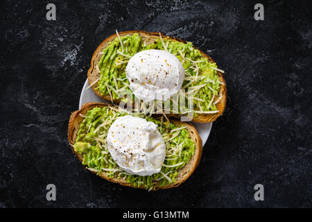 Zwei Toasts mit zerdrückte Avocado, Käse und Spiegelei auf dunklen strukturierten Hintergrund, Ansicht von oben. Gesundes Frühstück oder snack Stockfoto