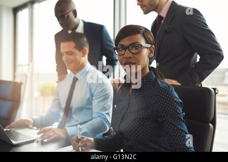 Attraktive ernst Geschäftsfrau trägt Brille und blaue Bluse mit drei männlichen Kollegen in fr am Konferenztisch sitzen Stockfoto