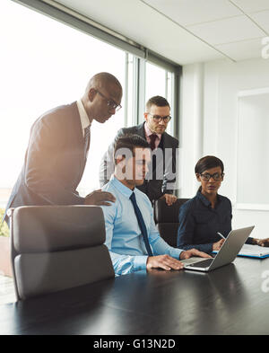 Gruppe von vier verschiedenen Männern und Frau sitzend am Konferenztisch mit leichten Flare in Ecke große Fenster in hellen Büro Stockfoto
