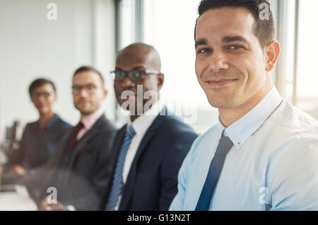 Heterogene Gruppe von vier grinsenden attraktive Business-Menschen sitzen am Tisch mit Rücken zur großen hellen Bürofenster mit leichten fl Stockfoto