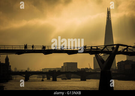 Pendler wandern bei Sonnenaufgang über eine Silhouette der Millennium Bridge mit dem Shard Gebäude und die Themse im Hintergrund zu arbeiten Stockfoto