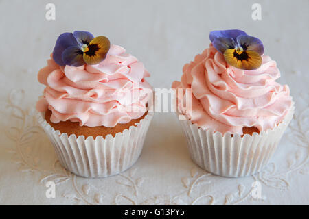 Hausgemachte rosa Zuckerguss Vanille Cupcakes mit essbaren Blüten Stockfoto