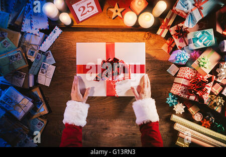 Santa Claus hält eine schöne Weihnachts-Geschenk-Box, Briefe und Geschenke rund um Hände Draufsicht Stockfoto