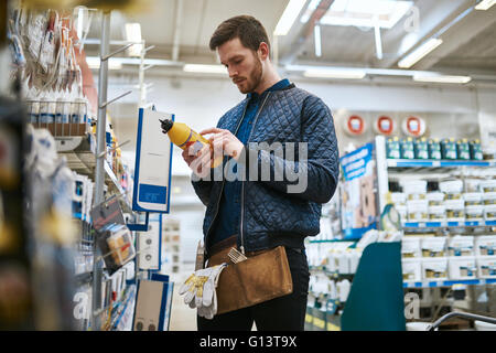 Handwerker, die seinen Kauf im Laden stehen lesen das Etikett auf ein Produkt im Hardwarebereich, niedrigen Winkel Ansicht auswählen Stockfoto