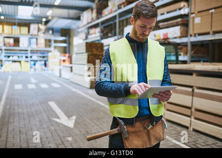 Junge Lager Arbeiter Umgang in Baubedarf stehend in einer Fahrt durch einen handheld-Tablet-Computer consulting Stockfoto