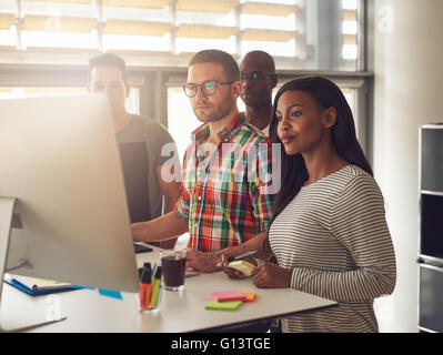 Gruppe von vier schwarzen, kaukasischen und hispanischen Erwachsenen Unternehmer tragen legere Kleidung stehen neben großen Computer di Stockfoto