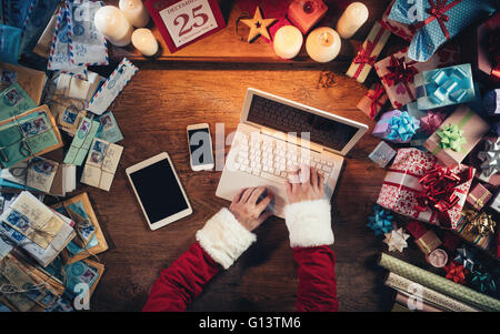 Hi-Tech-Weihnachtsmann arbeitet an seinem Schreibtisch und tippen auf einen Laptop, umgeben von Geschenk-Boxen und Weihnachten Briefe, Draufsicht Hände Stockfoto