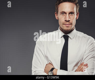 Heck grimmige Geschäftsmann mit verschränkten Armen starrte auf die Kamera mit einem intensiven Ausdruck, Oberkörper auf grau mit Textfreiraum Stockfoto