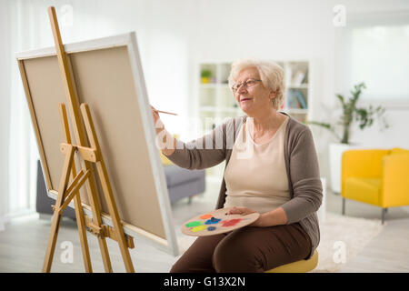 Reife Dame malen auf Leinwand mit einem Pinsel zu Hause Stockfoto