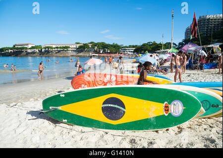 RIO DE JANEIRO - 5. April 2016: Brasilien Fahne stand Paddel Surfbrett Wartezeiten für Kunden am Strand der Copacabana. Stockfoto