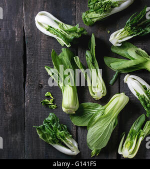 Sortiment der ganze und geschnittene rohe Baby Bok Choy (Chinakohl) über alten hölzernen Hintergrund. Dunkel rustikalen Stil. Ansicht von oben. Futtertrog Stockfoto