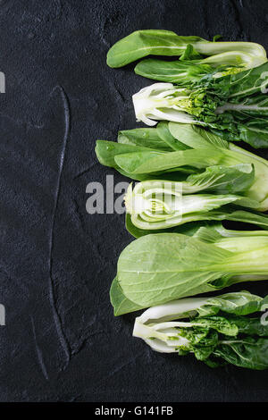 Sortiment der ganze und geschnittene rohe Baby Bok Choy (Chinakohl) über schwarzem strukturierten Hintergrund. Draufsicht mit Textfreiraum Stockfoto