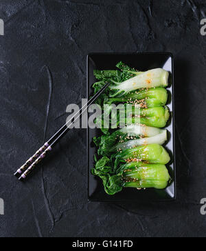 Gekochter Chinakohl mit Sesam Samen und Chili-Pfeffer Olivenöl im schwarzen Quadrat Keramikplatte mit schwarzen Stäbchen über schwarzer text Stockfoto