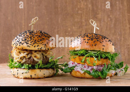 Hausgemachte traditionelle und Veggie Burger mit Rindfleisch, gebratenen Zwiebeln, süße Kartoffeln, Radieschen und Erbsen-Sprossen, diente über Holz Textur Stockfoto