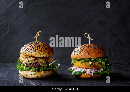 Hausgemachte traditionelle und Veggie Burger mit Rindfleisch, gebratenen Zwiebeln, süße Kartoffeln, Radieschen und Erbsen-Sprossen, serviert auf schwarz strukturiert Stockfoto