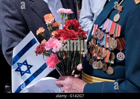 Ein sowjetischer jüdischer Veteran des Zweiten Weltkriegs mit festgeklemmten Medaillen In seiner alten Uniform hält er während der Zeremonie die israelische Flagge Kennzeichnung des alliierten Sieges über Nazi-Deutschland in Israel Stockfoto