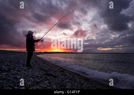 Ein Mann angeln im Meer am Strand bei Sonnenuntergang in Anglesey Stockfoto
