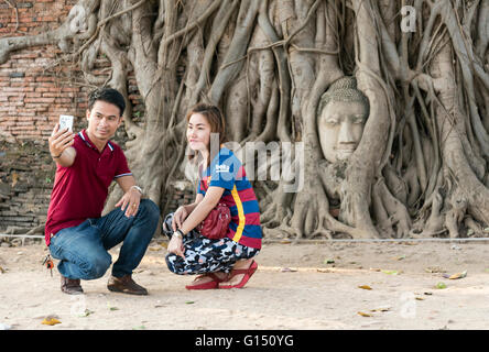 Besucher nehmen Selfie vor Buddha Kopf im Bodhi Baumwurzeln, Tempel Wat Mahathat, Ayutthaya, Thailand Stockfoto