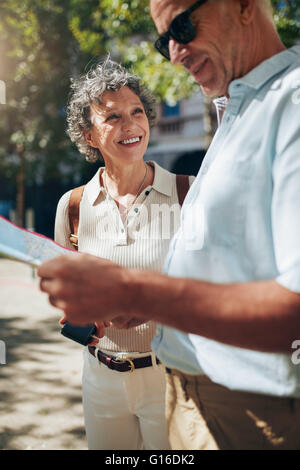 Älteres Paar mit Karte bei einem Spaziergang durch eine Stadt. Mann liest Karte und lächelnde Frau. Stockfoto