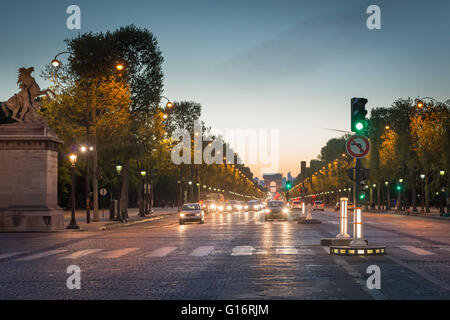 Überqueren Sie die Avenue des Champs Elysées und dem Arc de Triomphe in der Ferne, in der Dämmerung aufgenommen. Der Verkehr auf der Straße nähert sich Fußgängerüberweg. Stockfoto