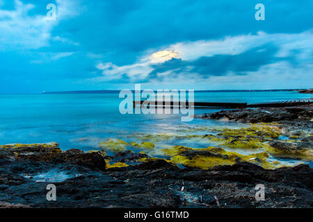 Ein Pier in Mitjorn-Strand, mit dem Leuchtturm auf dem Hintergrund der Es Cap de Barbaria. Formentera (Balearen). Stockfoto