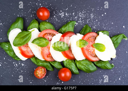 Frische italienische Caprese-Salat mit Mozzarella, Tomaten und Basilikum auf grauem Schiefer dunkel Stockfoto