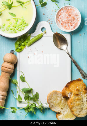 Sommerlich leichte grüne Creme Erbsensuppe in Schüssel mit Sprossen, Brot, Toast und Gewürze. Weiße Keramik Board in die Mitte, Türkis-bl Stockfoto