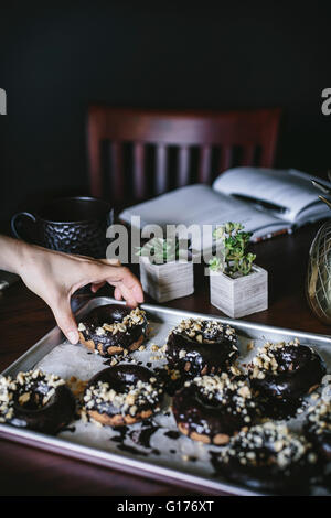 Eine Frau nimmt einen Donut aus einem Fach voller Schokolade glasierte Banane Brot Donuts. Stockfoto