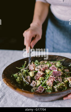 Eine Frau ist eine Schüssel mit Sesam Crusted gebratene Thunfischsalat mischen. Stockfoto