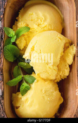 Hausgemachte Mango-Eis mit frischer Minze in Oliven Holz Schüssel serviert auf weißen Textilien Serviette über hölzerne strukturierten Hintergrund. Nach oben Stockfoto
