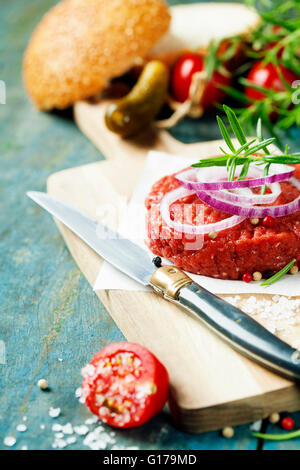 Rohes Rindfleischburger für Hamburger mit Gemüse auf Holztisch Stockfoto