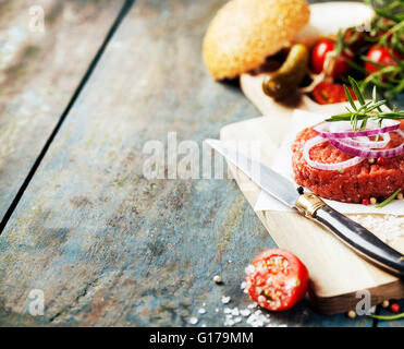 Rohes Rindfleischburger für Hamburger mit Gemüse auf Holztisch Stockfoto