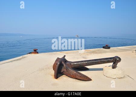 Alte rostige Schiff Anker auf Port mit Abfahrt Schiff im Hintergrund. Podgora, Kroatien Stockfoto