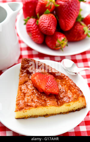 eine Platte mit einem Stück hausgemachter Käsekuchen garniert mit in Scheiben geschnittenen Erdbeeren und eine Platte mit reife Erdbeeren auf einem Tisch set mit Stockfoto