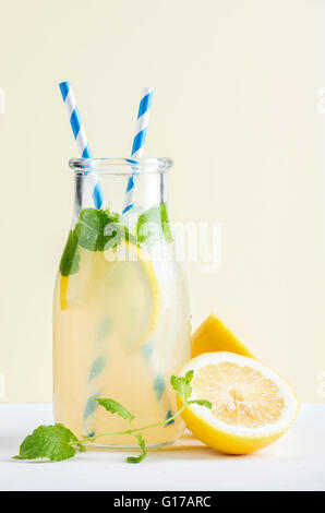 Flasche hausgemachten Limonade mit Eis und Zitronen, Papier Strohhalme und Pastell gelb hinterlegt, selektiven Fokus Stockfoto