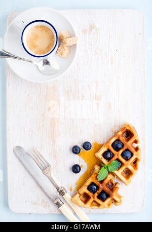 Espresso Kaffee Tasse und weiche belgische Waffeln mit frischen Heidelbeeren und Marple Sirup auf weiß lackiertem Holzbrett über leichte bl Stockfoto