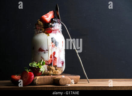 Joghurt-Hafer-Müsli mit Erdbeeren, Maulbeeren, Honig und Minze Blätter in Longdrinkglas Glas auf schwarzem Hintergrund, Tiefenschärfe, co Stockfoto