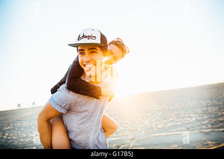 Junger Mann mit Freundin eine Huckepack am sonnigen Strand, Venice Beach, Kalifornien, USA Stockfoto