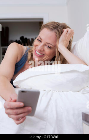 Frau liest Smartphone Texte im Bett Stockfoto