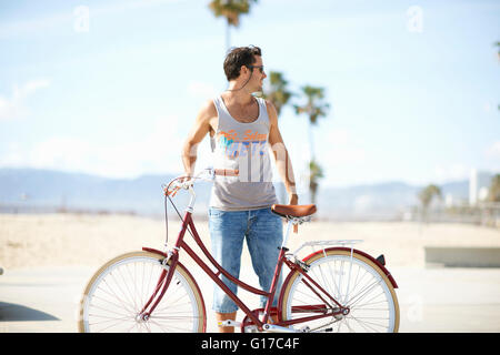 Mann auf der Suche zurück, während Radfahren am Venice Beach, Los Angeles, Kalifornien, USA Stockfoto