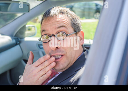 Mann im Auto tragen Brillen, Hand über Mund, Blick in die Kamera Stockfoto