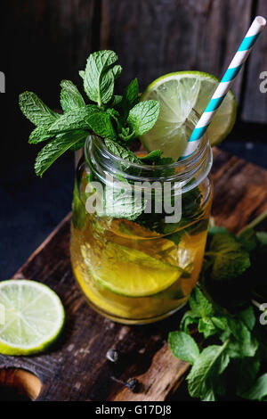 Grüner Eistee mit Eis, frische Minze, Limette und Zitrone im Glas Einmachglas mit Retro-cocktail, serviert auf Schneidbrett aus Holz Stockfoto