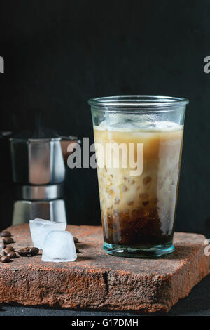 Glas Eiskaffee mit Sahne und Milch, serviert mit Kaffeebohnen, Eiswürfel und Kaffeekanne auf Steinplatte über schwarze strukturierte b Stockfoto