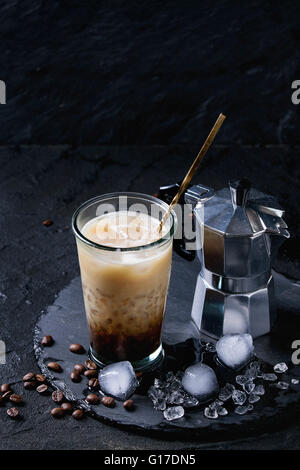 Glas Eiskaffee mit Sahne und Milch, serviert mit Kaffeebohnen, Eiswürfel und Kaffeekanne auf Schiefer Steinplatte über schwarzer text Stockfoto